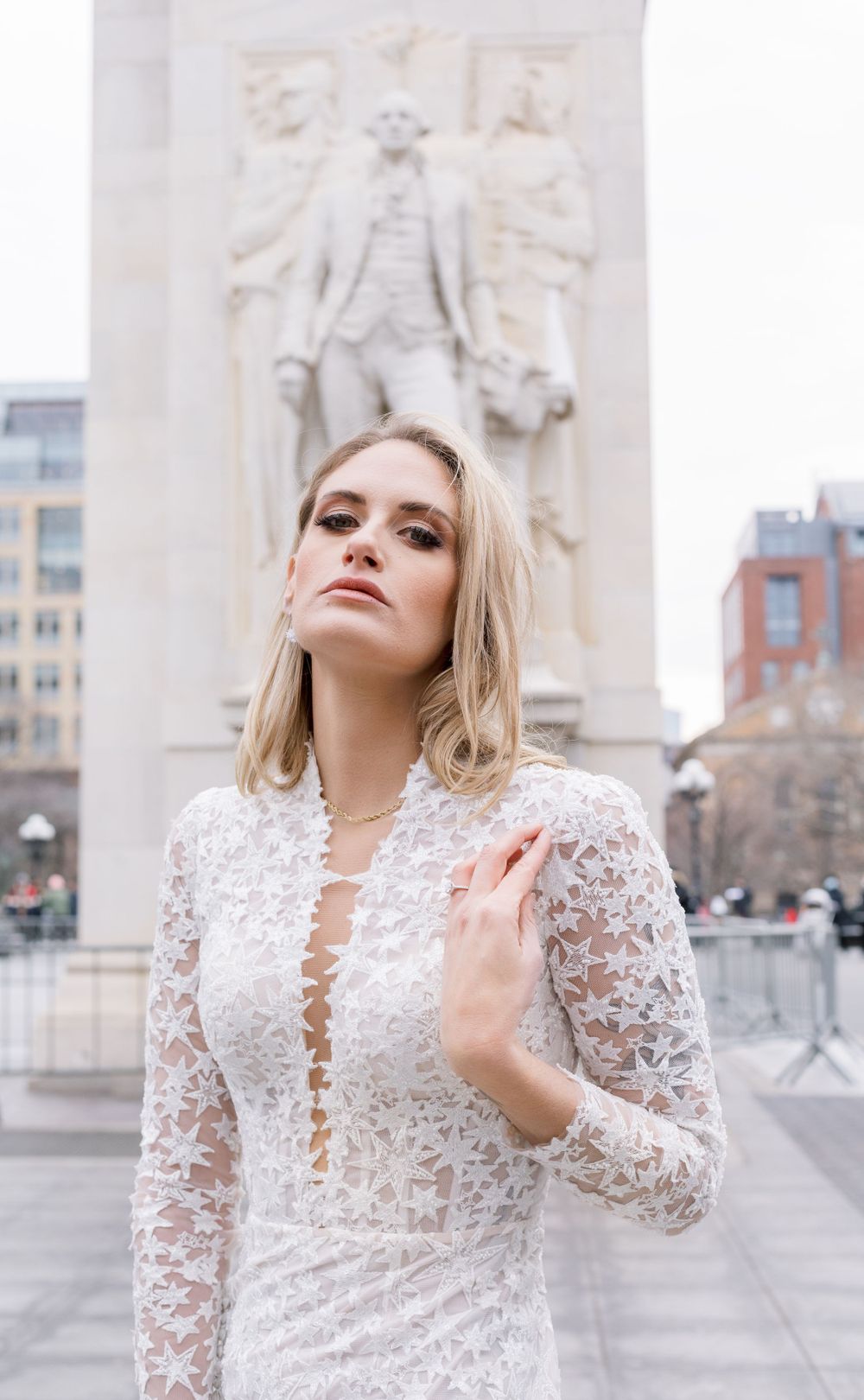 Bride in detailed lace gown poses in front of historic monument in urban setting.