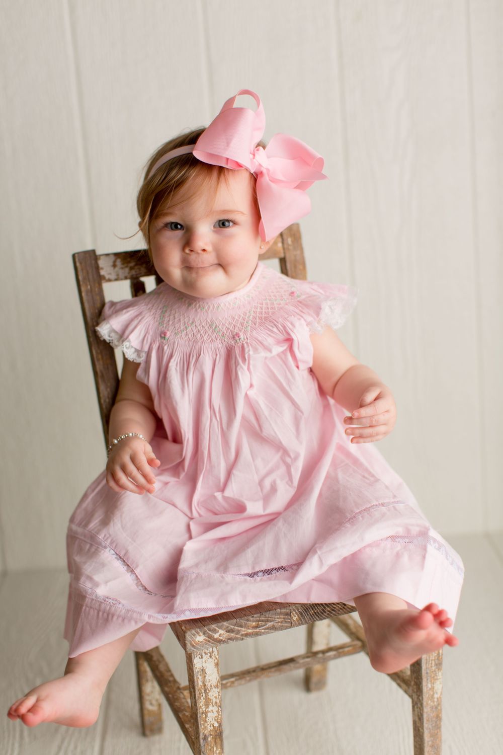 Small child in pink smock dress sitting on vintage wooden chair.