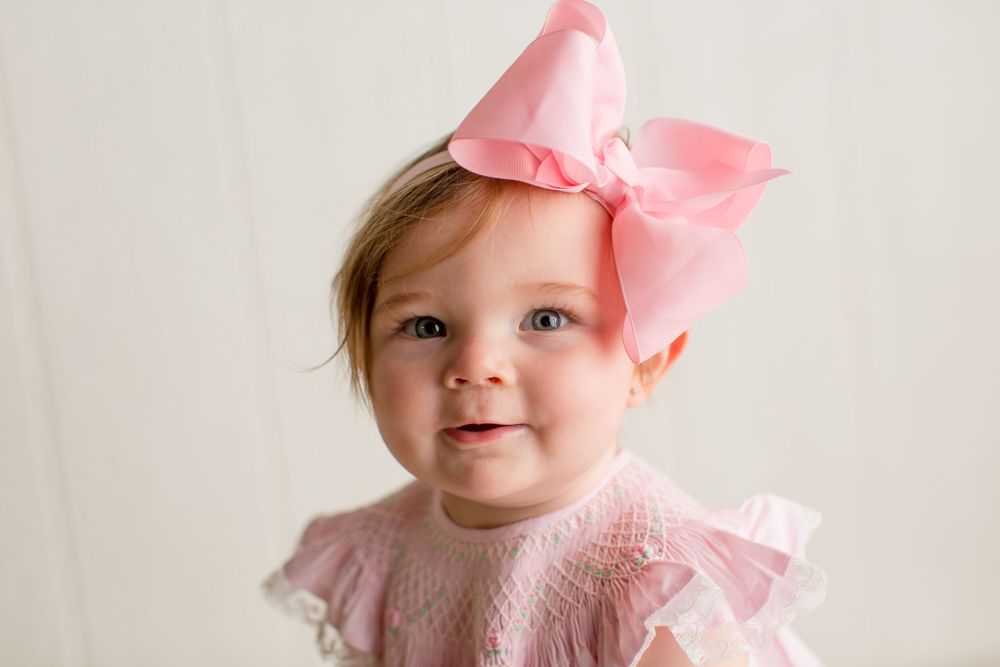 Small child in pink dress with matching bow against white background.