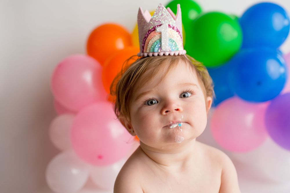 Party crown and rainbow balloon arch create festive birthday photo setting.