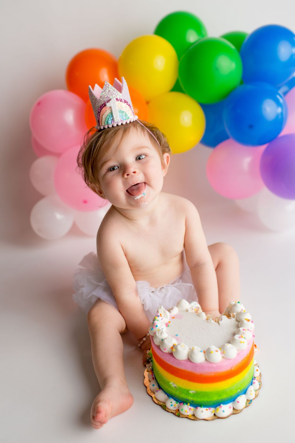 Joyful birthday celebration with rainbow cake and vibrant balloon arch backdrop.