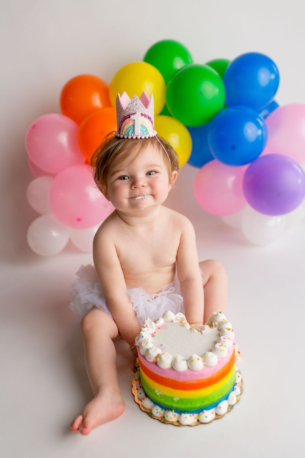 Rainbow cake and balloon arch create colorful birthday photo backdrop.