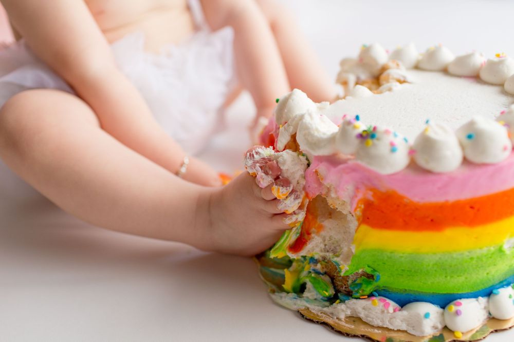 Close-up of small hands touching rainbow layer cake with white frosting.