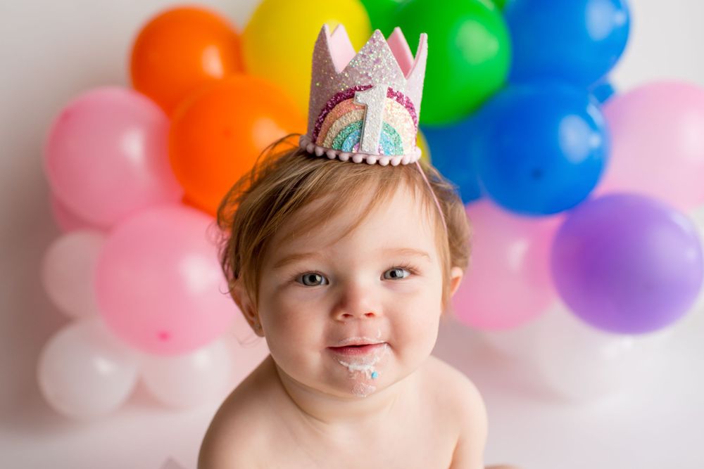 Festive crown and rainbow balloon arch create magical birthday setting.