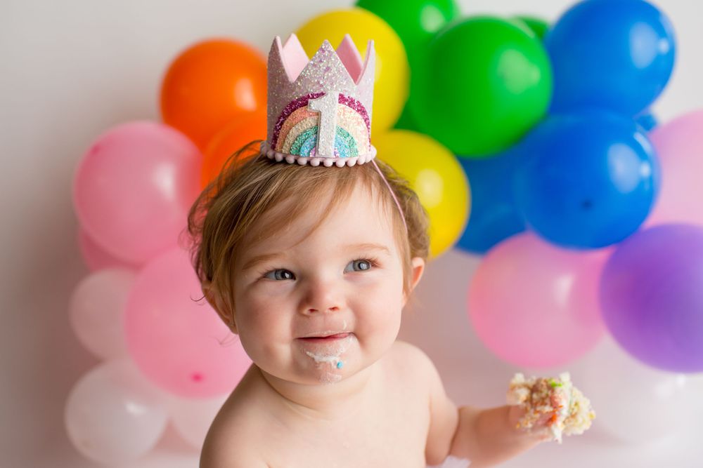 A cheerful cake smash photo with rainbow balloons and a unicorn party crown.