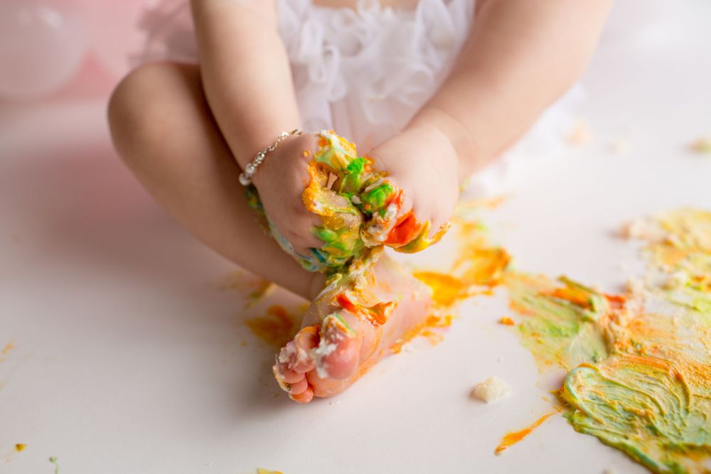 Close-up of small hands covered in colorful cake frosting during a cake smash.