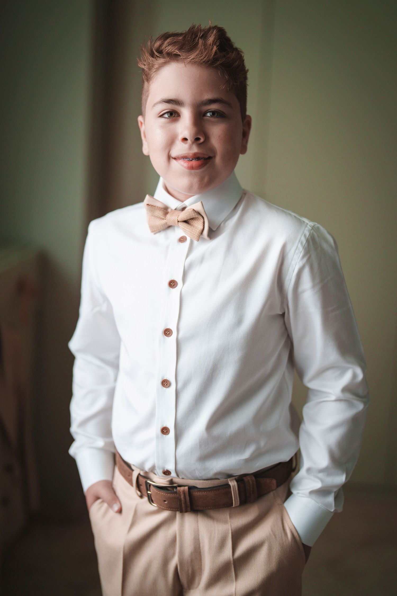 A portrait of someone wearing a white dress shirt and peach bow tie with a gentle smile.