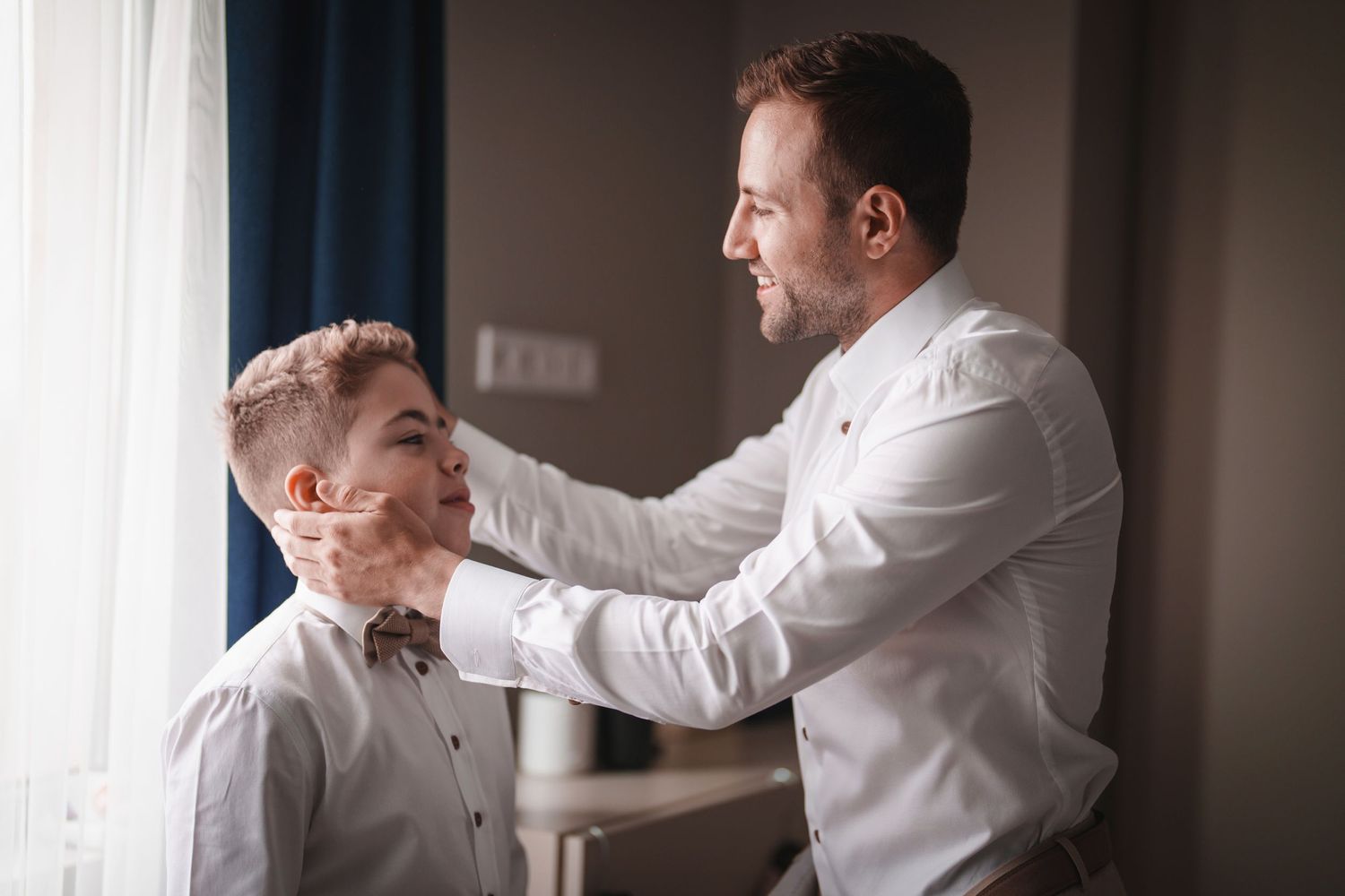 A tender moment as someone helps adjust a bow tie in natural window light.