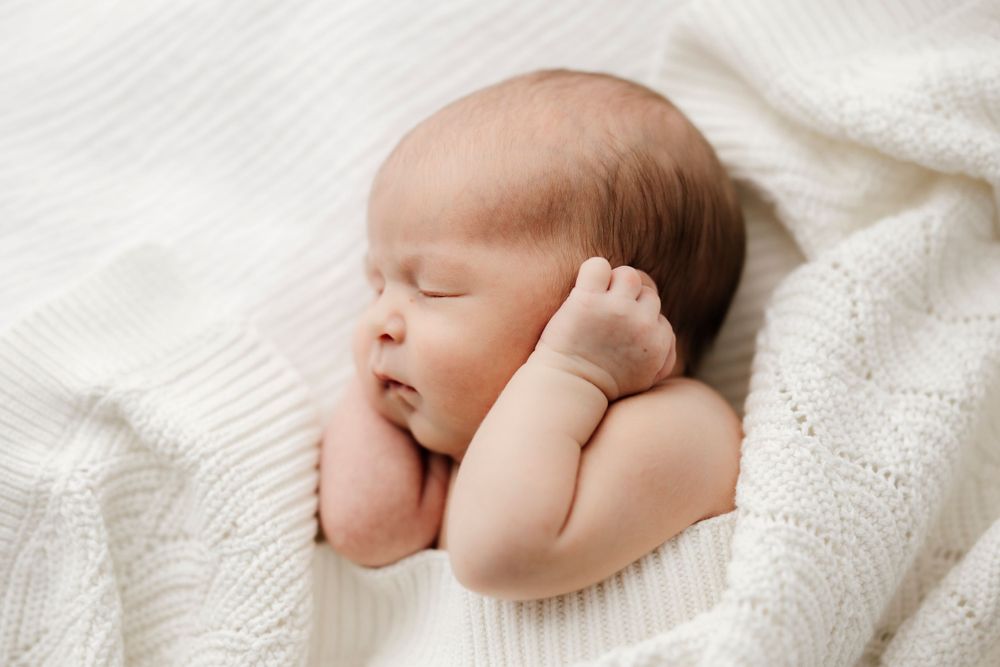 Peaceful newborn baby sleeping soundly on white blanket.