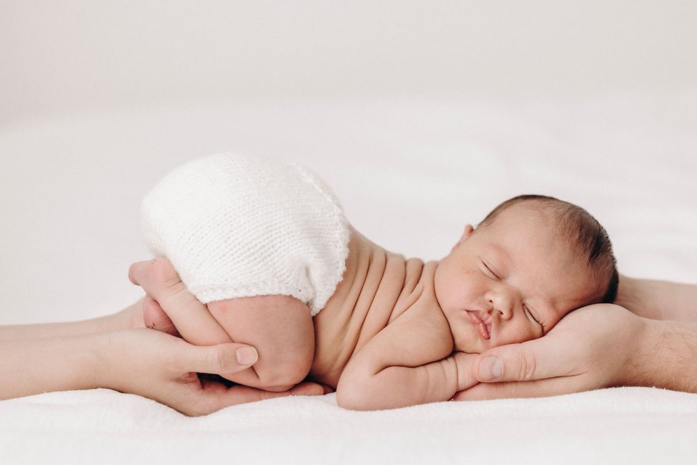 Sleeping newborn wrapped in white fabric on light background.
