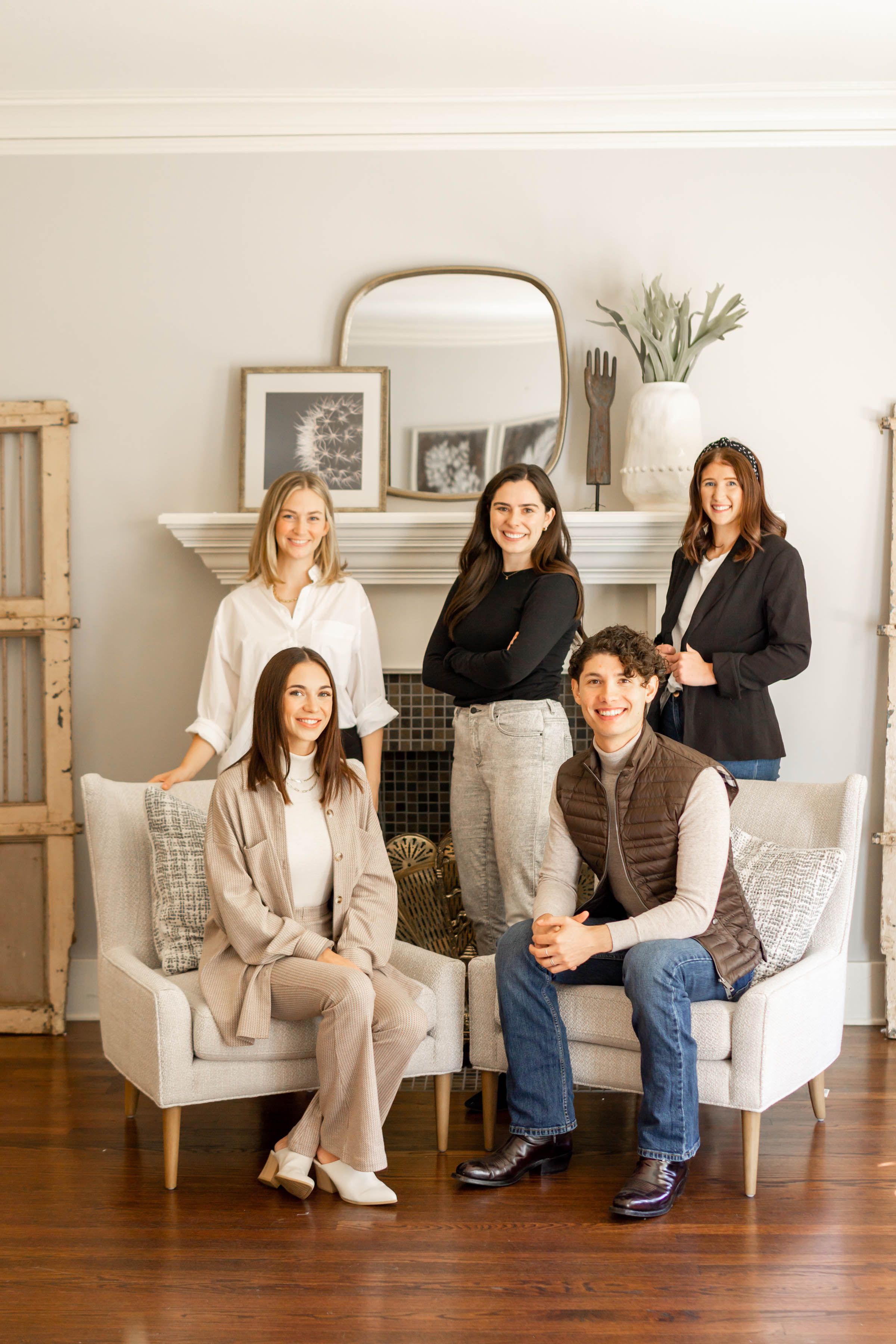 Professional real estate team of five posing in elegant living room with fireplace.