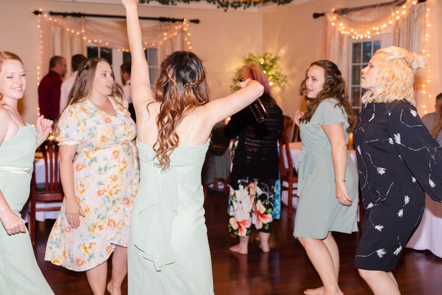 Wedding party dancing and celebrating in a decorated reception hall with string lights.
