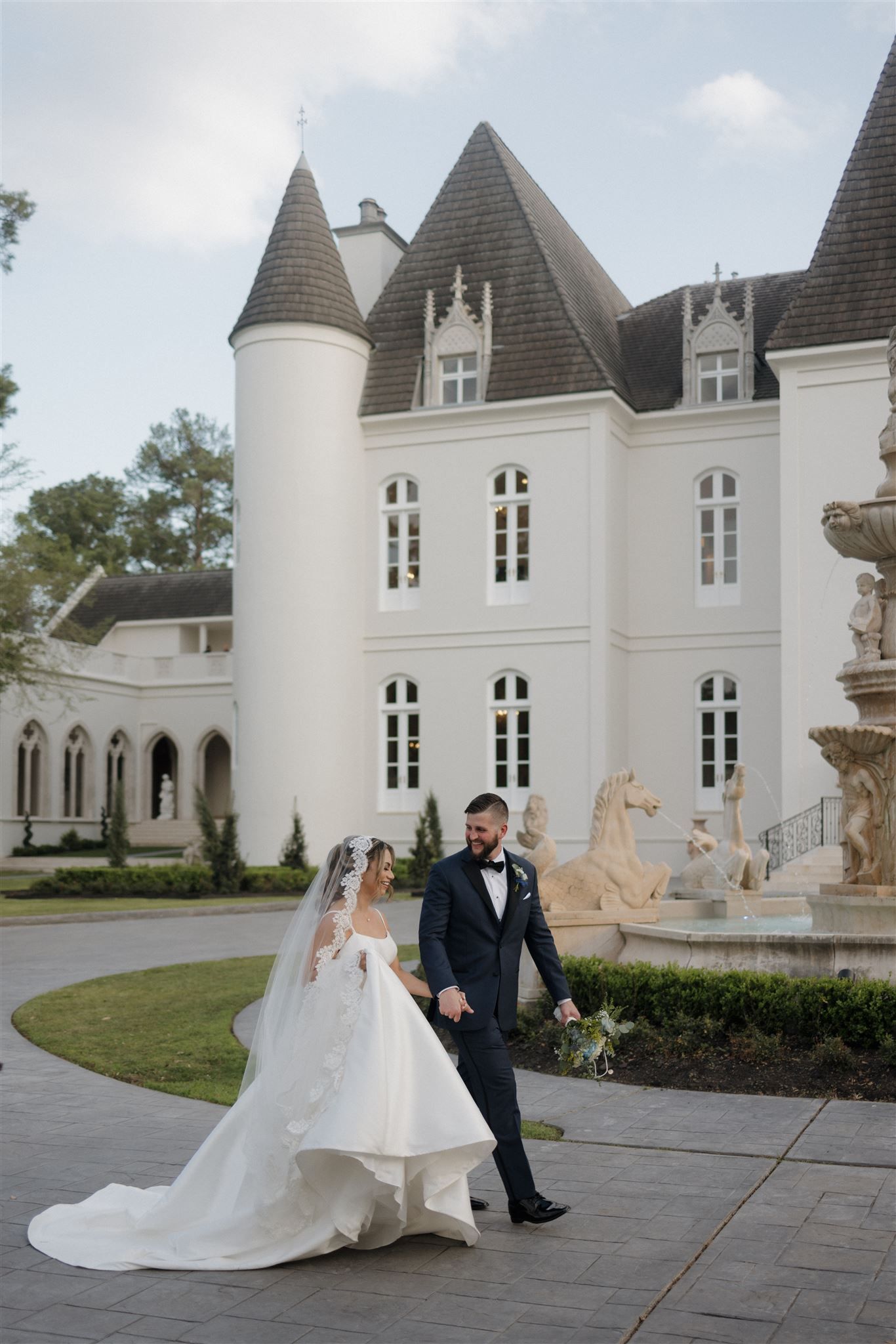 Couple walks in front of stunning white castle-like venue with turrets and ornate architecture.