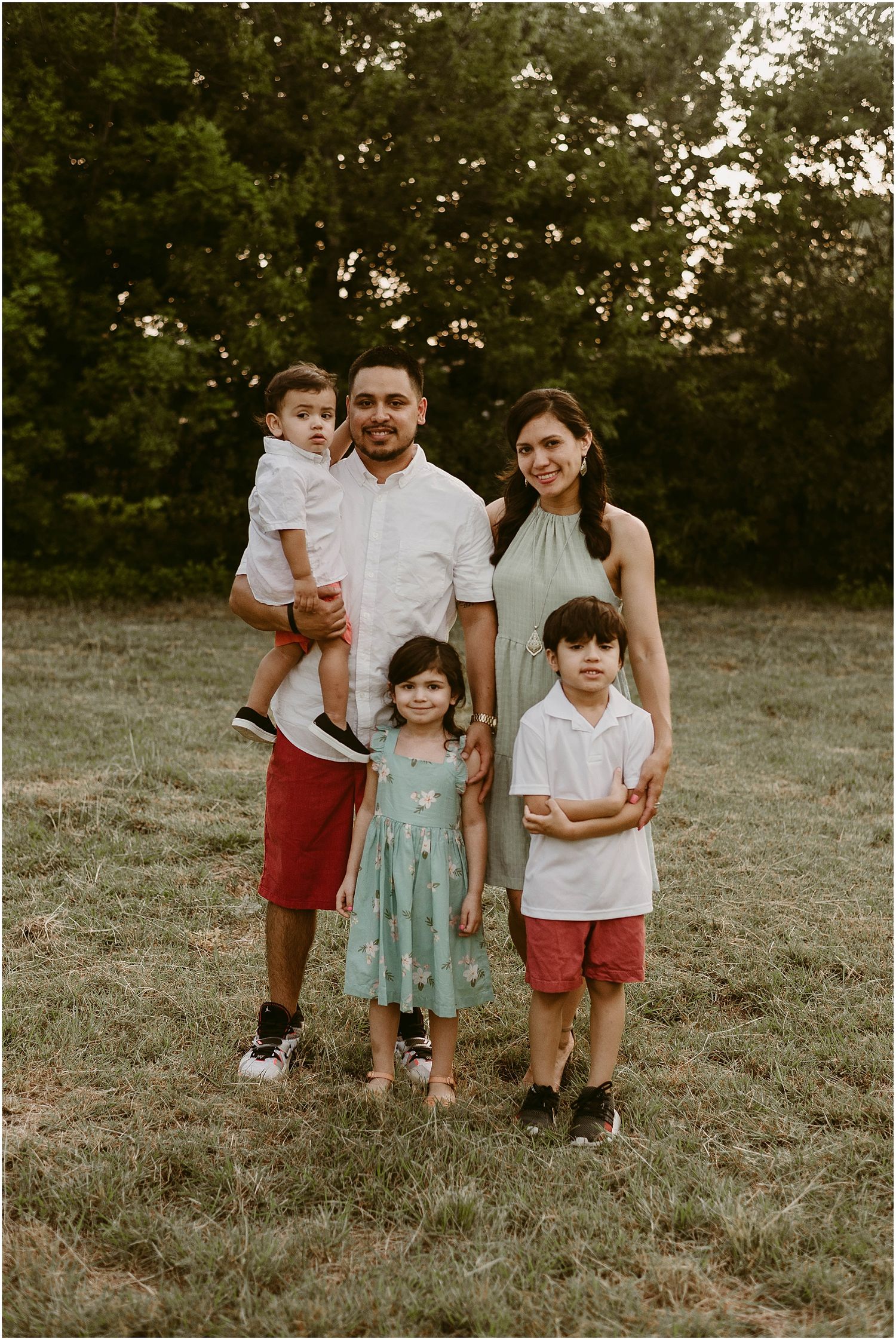 A family stands together in a grassy field at sunset.