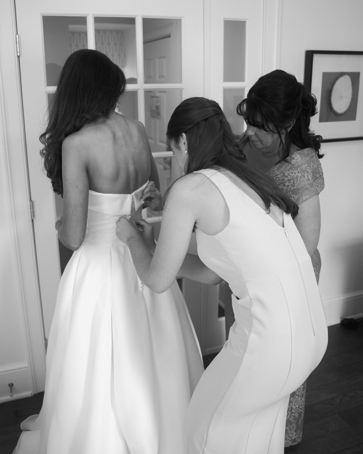Wedding dress preparation scene showing helpers assisting with the gown.