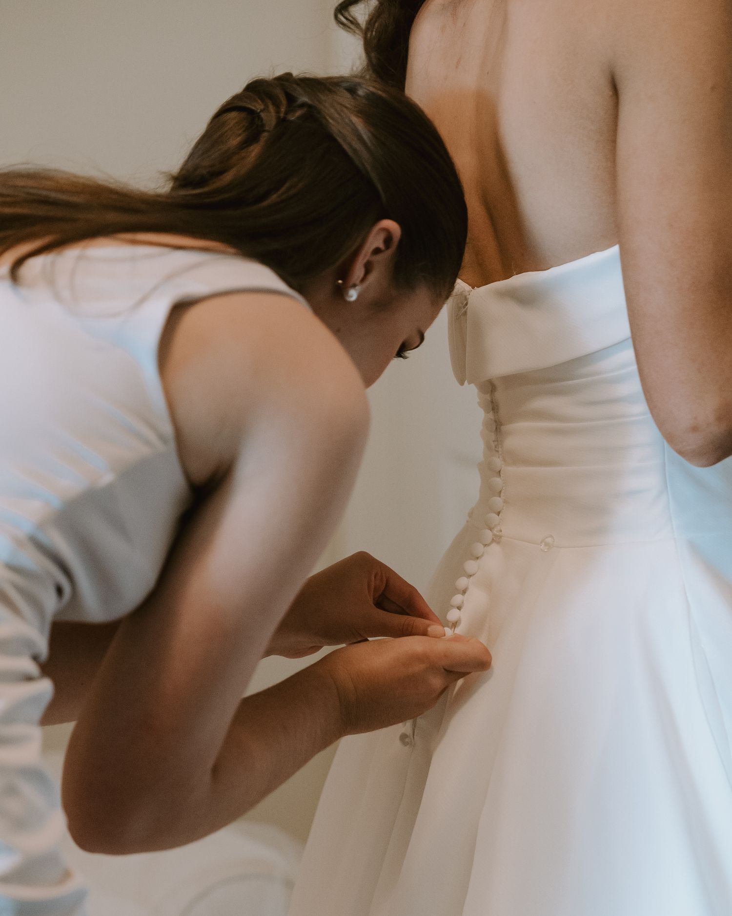 Detailed shot of dress buttons being fastened on a white wedding gown.
