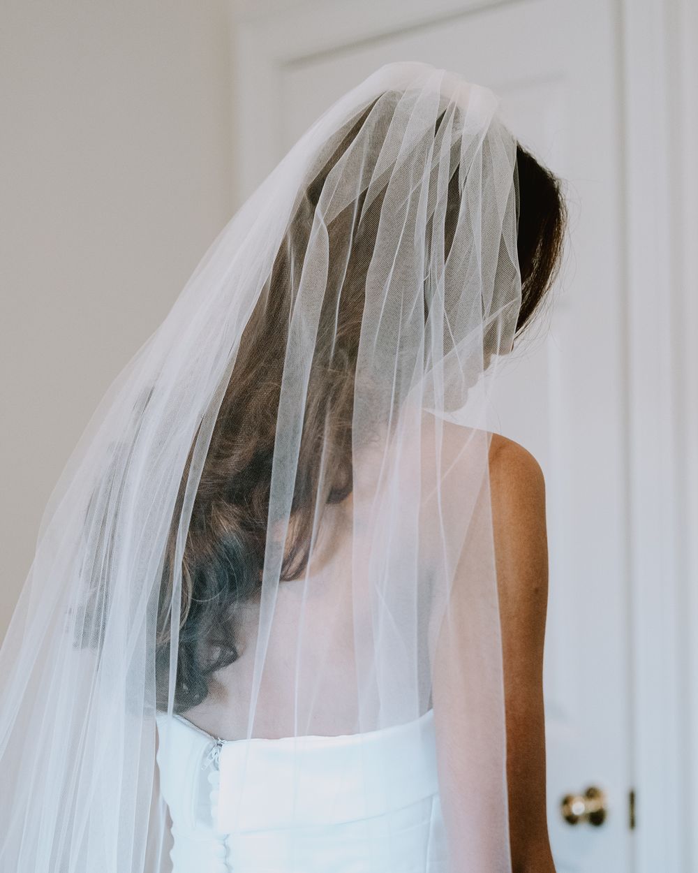 Back view of a flowing white wedding veil against a light background.