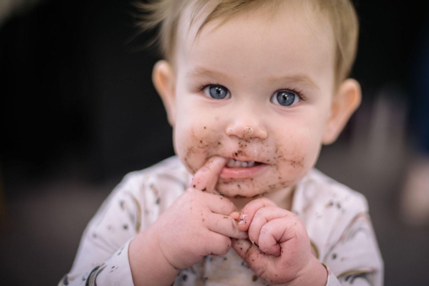 Baby with chocolate-covered face and bright blue eyes smiles at camera.
