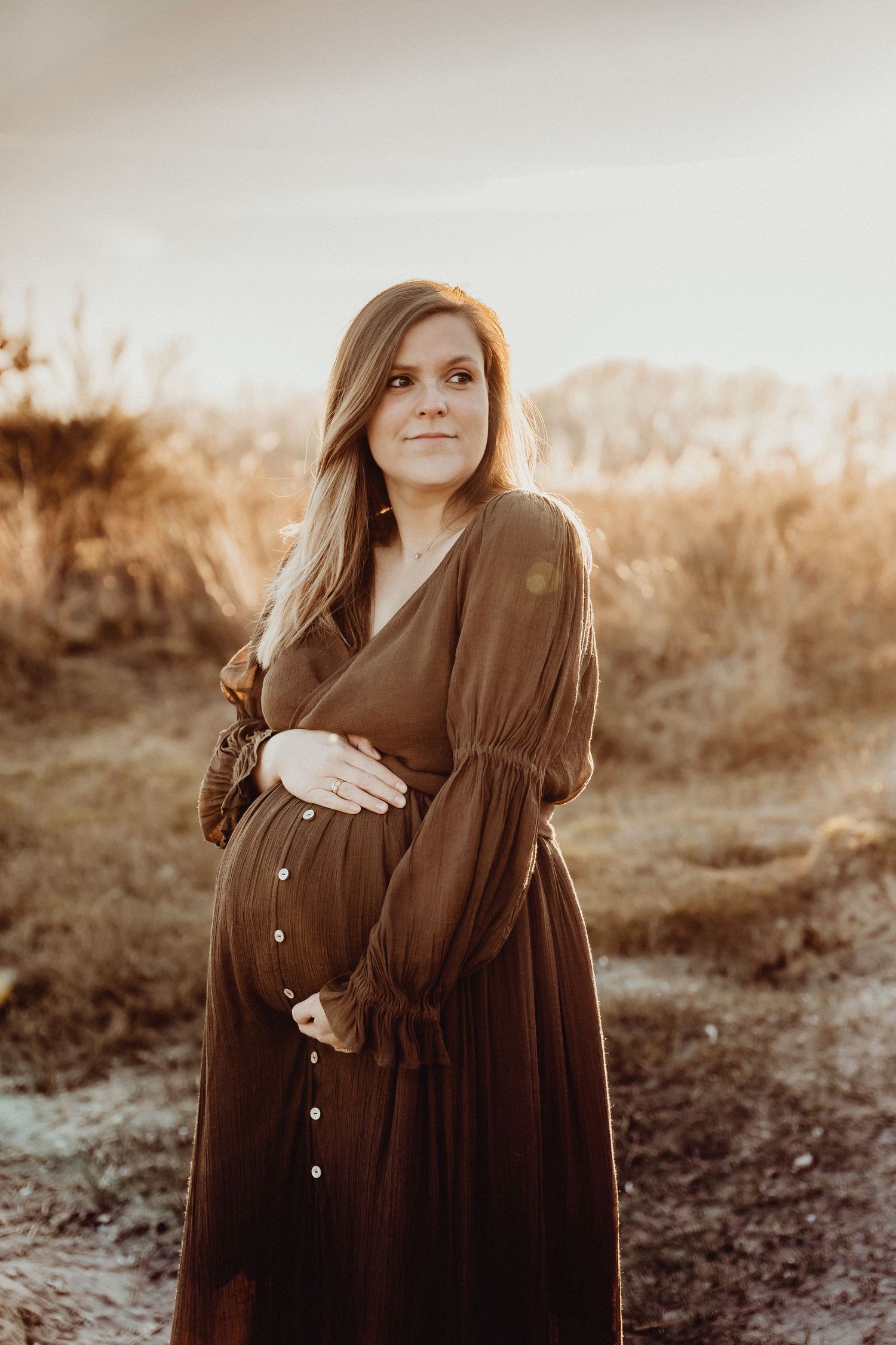 Silhouette against golden light wearing long brown dress in natural setting.