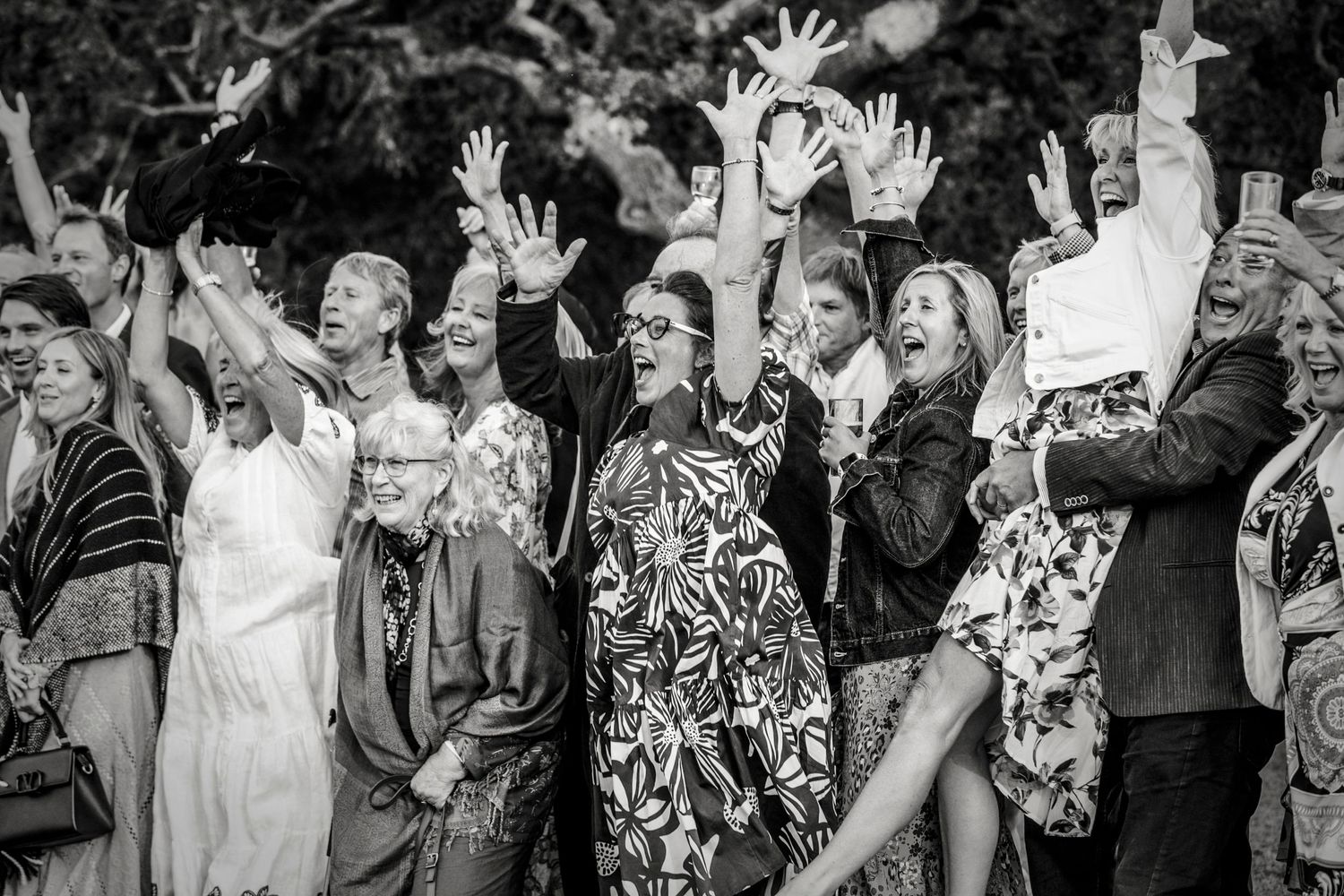 Wedding guests dance and celebrate with raised hands in black and white photography.