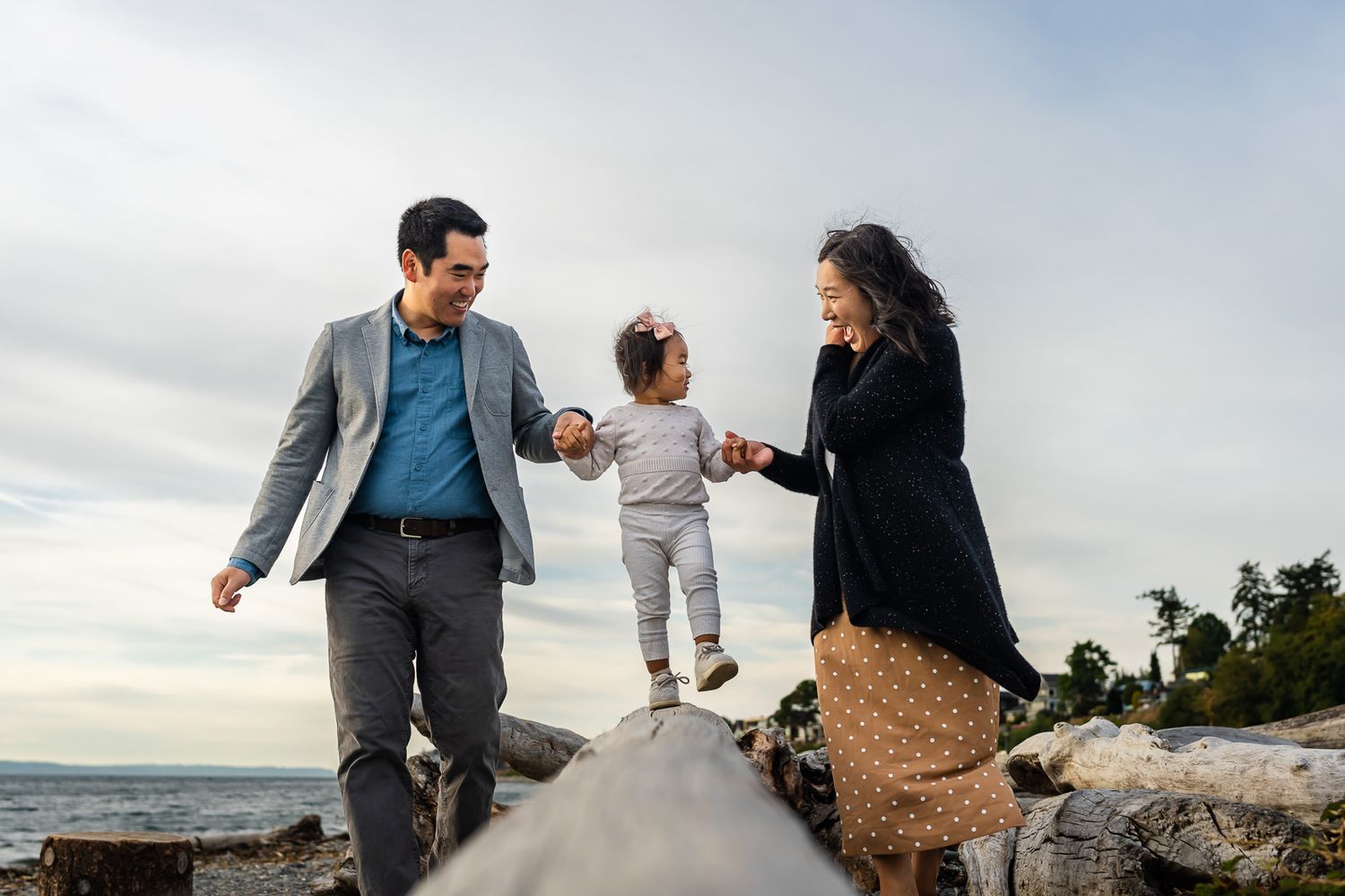 Parents hold daughter's hand while she walks on driftwood in Shoreline.