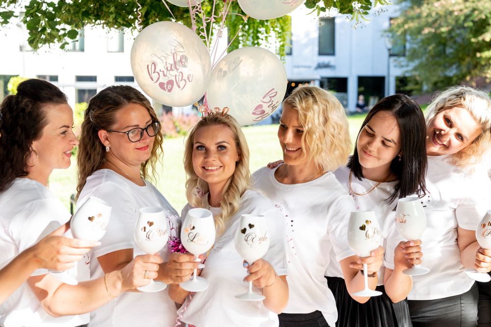 Friends celebrate together holding white balloons and cups in matching outfits.