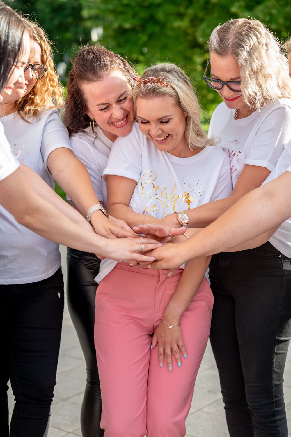 Group huddle of friends wearing matching white t-shirts and laughing together outdoors.
