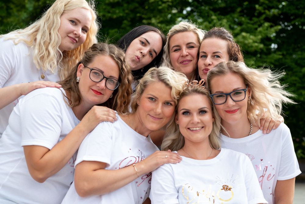 A group in matching white t-shirts poses together playfully for a cheerful outdoor photo.