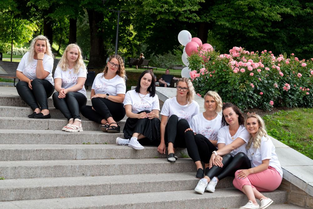 A group sits casually on outdoor stone steps with pink balloons and flowers in the background.