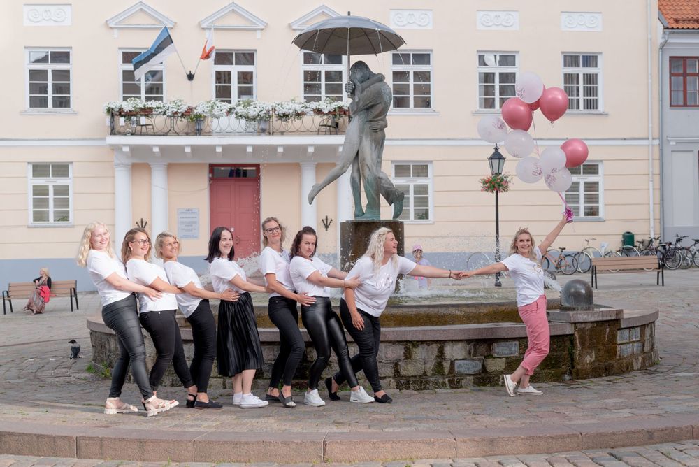 Friends pose playfully by a statue and fountain in matching outfits with pink and white balloons.