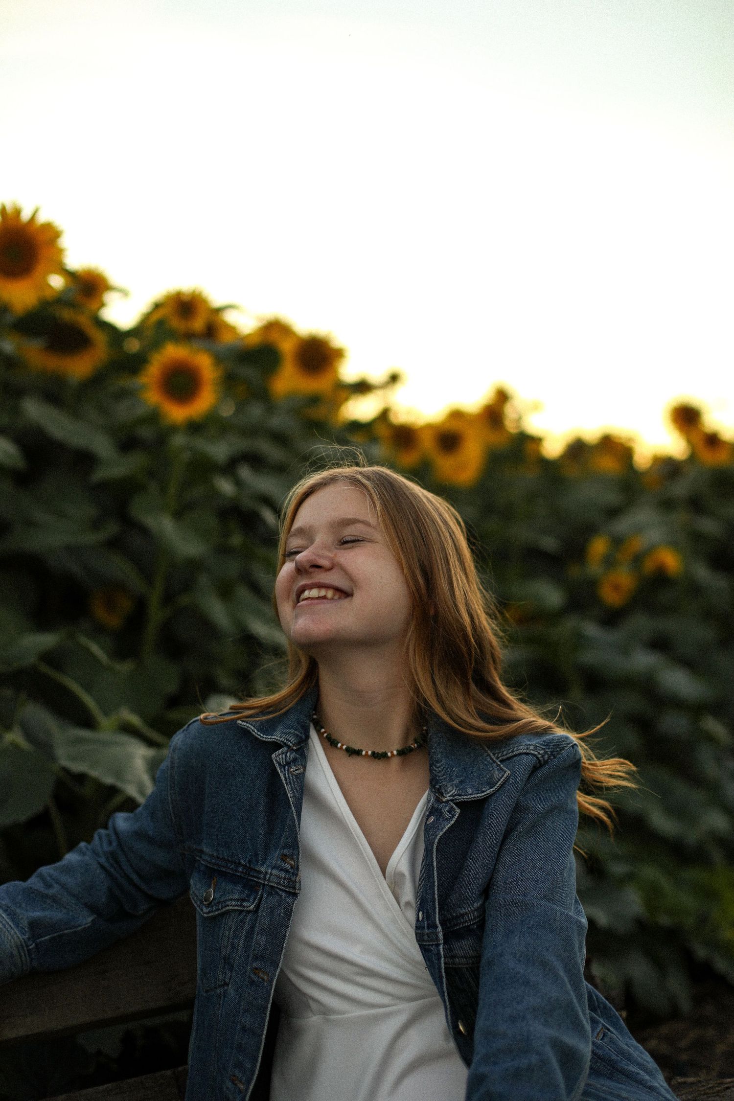 Candid portrait in sunflower field at sunset with denim jacket and natural lighting.