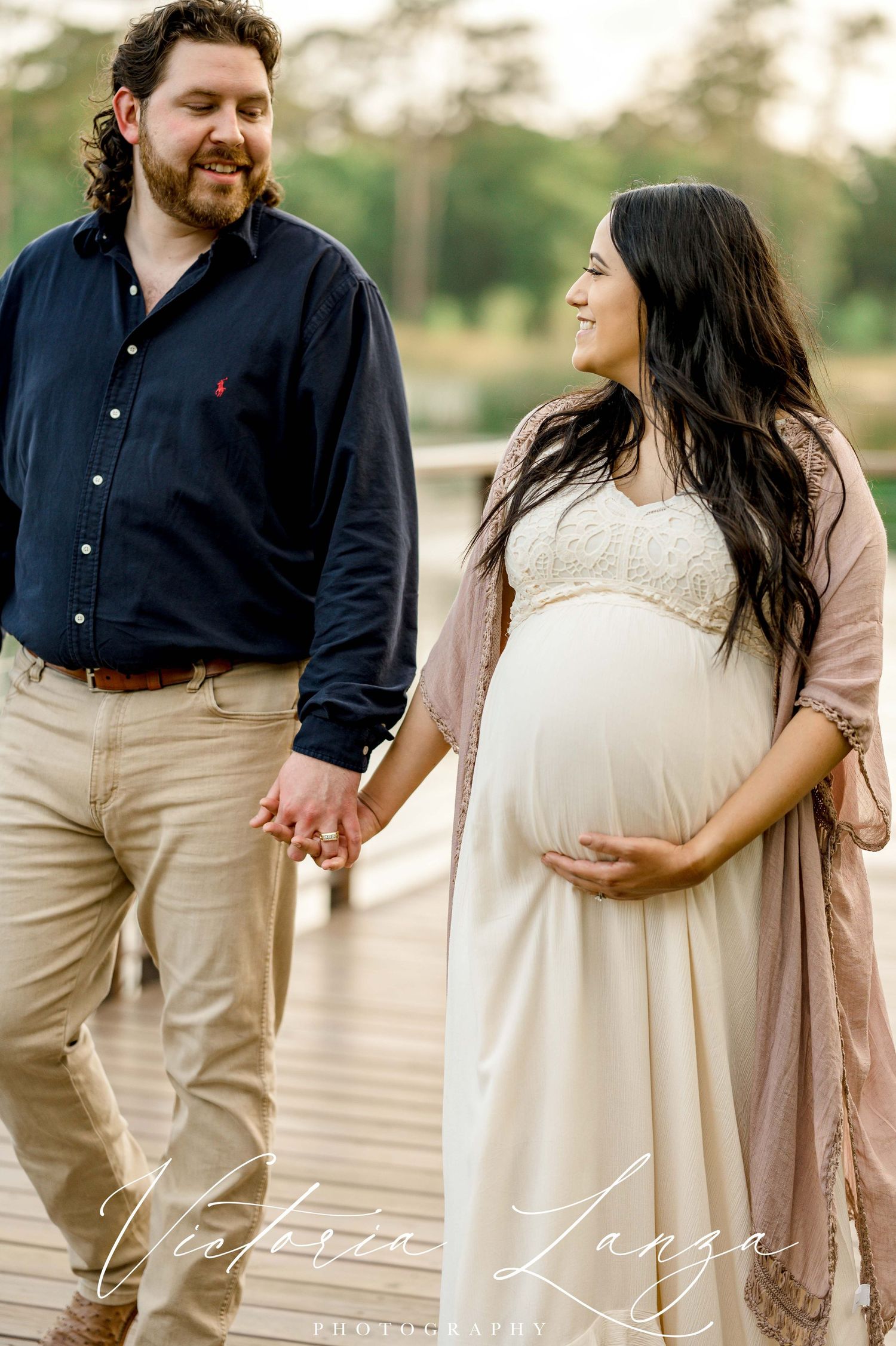 couple casually walking on a bridge while taking maternity photos in HOUSTON texas at memorial park