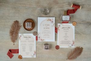 Elegant wedding stationery flat lay with floral designs and feather accents in coral and white.