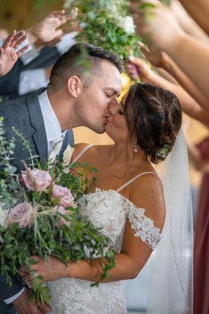 Intimate wedding kiss moment with floral bouquet and greenery decorations.