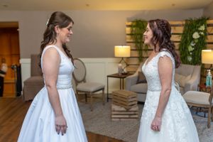 Two women in white wedding dresses sharing a meaningful moment in an elegant indoor setting.