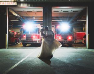 A romantic silhouette dances in front of illuminated fire trucks in a dimly lit garage.