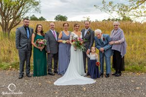 Wedding party in formal attire posing together in a field with autumn colors.