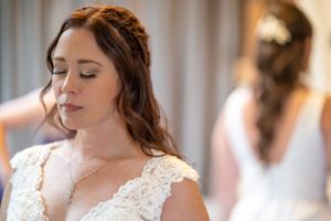 Bride with braided hair and lace dress detail in soft indoor lighting.