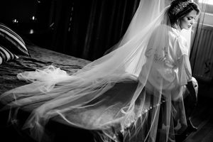 Dramatic black and white photo of bride with flowing veil during wedding preparations.