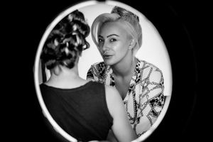 Black and white artistic portrait reflected in a mirror showing a floral blouse and vintage hairstyle.