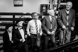 Black and white photo of men seated in a church pew with varying expressions.