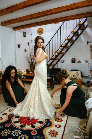 Wedding dress fitting scene with floral patterned rug and rustic wooden staircase in the background.