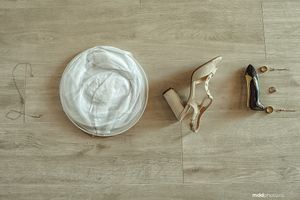 Wedding details flatlay with dress, shoes and miniature figurines on wooden floor.