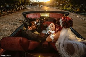 Newlyweds sharing tender moment in classic convertible car during golden sunset.