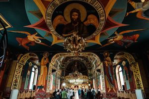 Orthodox church interior with ornate ceiling frescoes and religious iconography during ceremony.