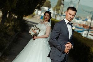 Elegant wedding couple poses in formal attire near a marina with boats in the background.
