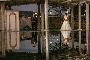 Creative wedding photo with reflection of couple in formal attire standing on mirrored surface.
