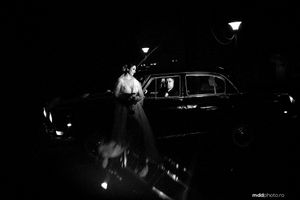 Dramatic black and white nighttime portrait with vintage car and street lighting.