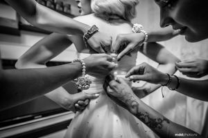 Multiple hands helping with wedding dress preparations in black and white.