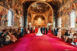Ornate church ceremony with red carpet aisle and beautiful fresco paintings on walls and ceiling.